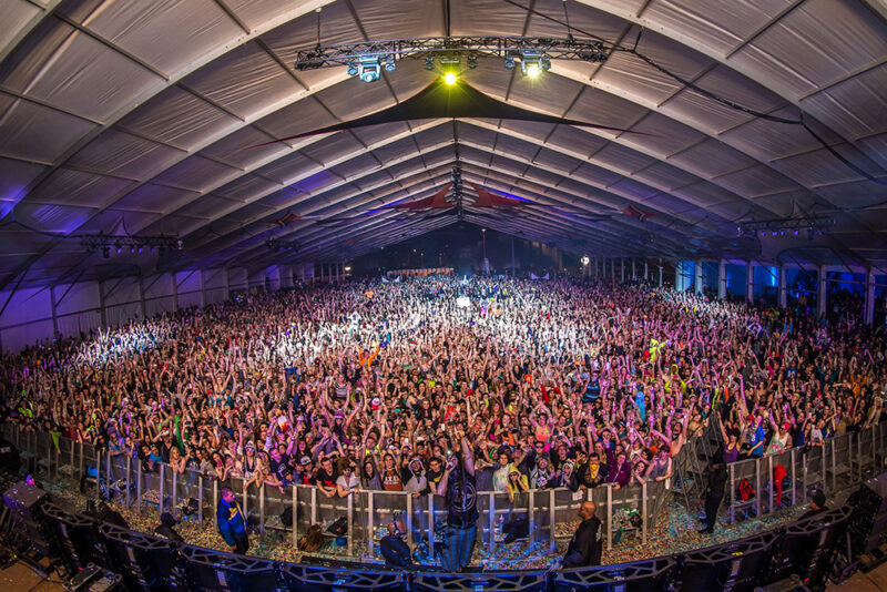 Facing a crowd of people at music festival under a tent.