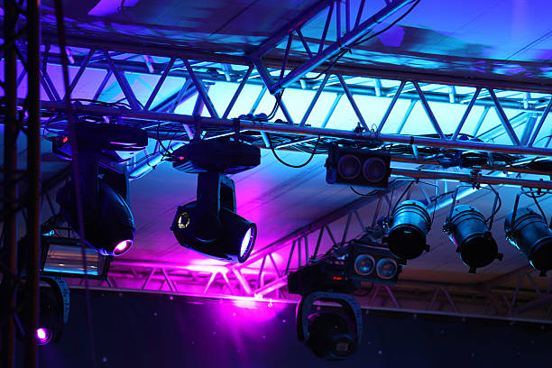 Stage lights flooding a theather at an entertainment event, with blue and purple light beams, lighting equipments and steel structures.